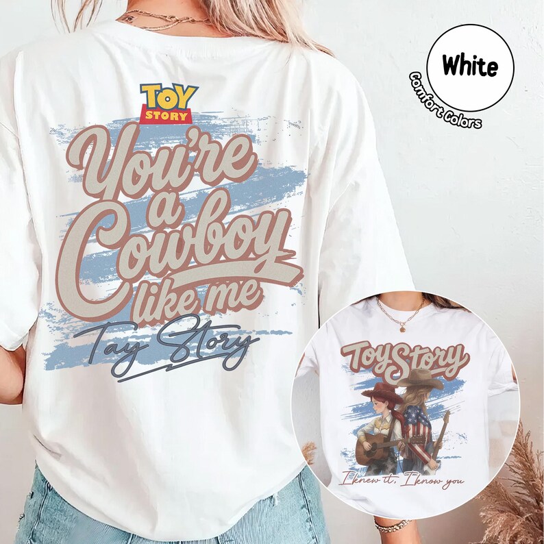 May include: A white t-shirt featuring a large graphic on the back with the text "Toy Story" and "You're a Cowboy like me Tay Story" in brown and blue. A circular inset shows the same shirt with a graphic of two figures and a guitar.