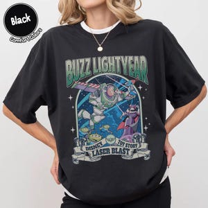 Puede incluir: Camiseta negra con un gr&aacute;fico de Buzz Lightyear de Toy Story. El dise&ntilde;o incluye el texto "Buzz Lightyear" sobre una imagen del personaje en vuelo, con "Disney Toy Story Laser Blast" debajo. La camiseta es de la marca Comfort Colors.