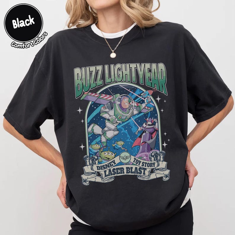 Puede incluir: Camiseta negra con un gr&aacute;fico de Buzz Lightyear de Toy Story. El dise&ntilde;o incluye el texto "Buzz Lightyear" sobre una imagen del personaje en vuelo, con "Disney Toy Story Laser Blast" debajo. La camiseta es de la marca Comfort Colors.