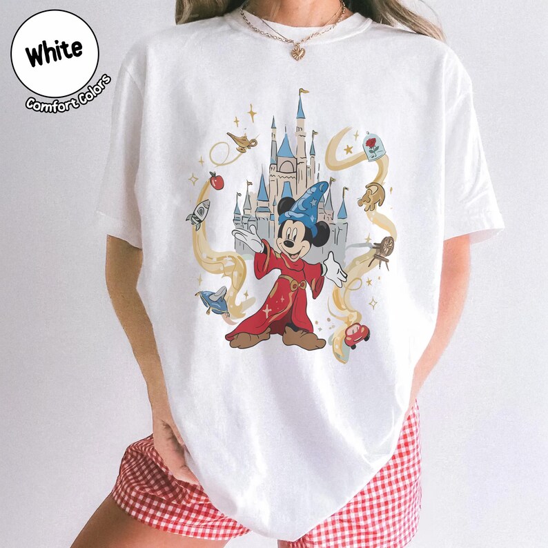 May include: White t-shirt with a vibrant graphic of Mickey Mouse as a sorcerer, surrounded by animated imagery and a castle. The text "White Comfort Colors" is in a circle at the top left.