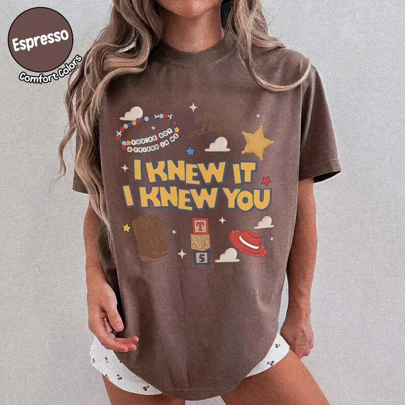 Puede incluir: Una camiseta marr&oacute;n de manga corta con un estampado gr&aacute;fico que incluye el texto I KNEW IT I KNEW YOU, una pulsera de cuentas con el texto YOU'VE GOT A FRIEND IN ME, una bota vaquera marr&oacute;n, un sombrero rojo y bloques apilados con T, S y 5.
