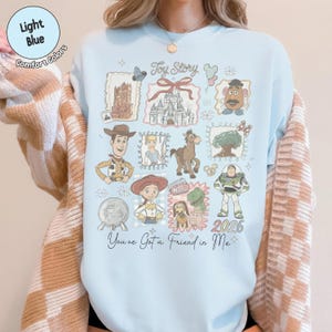 May include: Light blue sweatshirt featuring a collage of Toy Story characters and imagery. The design includes Woody, Buzz Lightyear, Jessie, and other characters, along with the text "Toy Story" and "You've Got a Friend in Me."