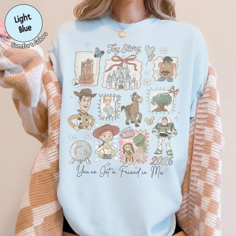 May include: Light blue sweatshirt featuring a collage of Toy Story characters and imagery. The design includes Woody, Buzz Lightyear, Jessie, and other characters, along with the text "Toy Story" and "You've Got a Friend in Me."
