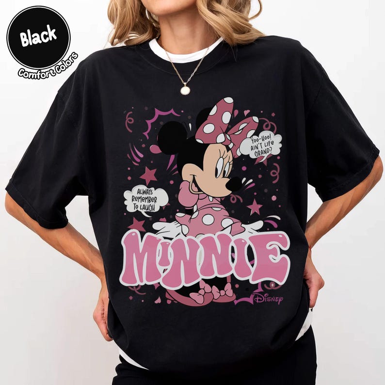 May include: Black t-shirt featuring Minnie Mouse in a pink polka-dot dress and bow. The design includes the word "MINNIE" in pink bubble letters, speech bubbles, and the text "Always Remember To Laugh".