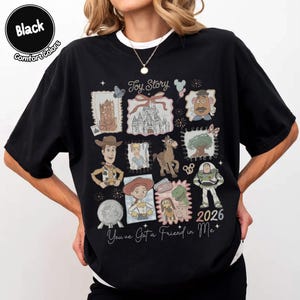 May include: Black t-shirt featuring a collage of Toy Story characters and imagery. The design includes Woody, Buzz Lightyear, and other characters, along with the text "Toy Story" and "You've Got a Friend in Me". The year "2026" is also displayed.