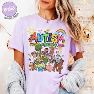 K&ouml;nnte beinhalten: Ein helllila T-Shirt mit einem farbenfrohen Aufdruck mit dem Wort "AUTISMUS" und dem Satz "akzeptieren verstehen lieben". Die Grafik enth&auml;lt einen Regenbogen, eine Sonne und verschiedene Zeichentrickfiguren. Das Shirt hat kurze &Auml;rmel.