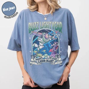 Puede incluir: Camiseta azul vaquero Comfort Colors con un gr&aacute;fico de Buzz Lightyear de Toy Story. El dise&ntilde;o incluye el texto "BUZZ LIGHTYEAR" y "DISNEY TOY STORY LASER BLAST" con im&aacute;genes de los personajes.