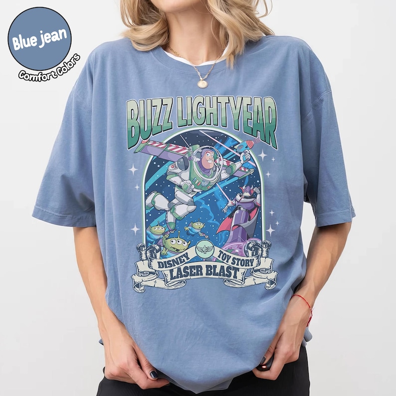 Puede incluir: Camiseta azul vaquero Comfort Colors con un gr&aacute;fico de Buzz Lightyear de Toy Story. El dise&ntilde;o incluye el texto "BUZZ LIGHTYEAR" y "DISNEY TOY STORY LASER BLAST" con im&aacute;genes de los personajes.