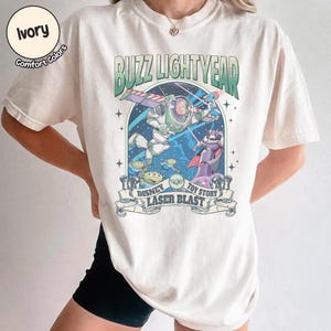 Puede incluir: Camiseta de color marfil con un gr&aacute;fico de Buzz Lightyear de Toy Story. El dise&ntilde;o incluye el texto "Buzz Lightyear", "Disney" y "Laser Blast". La camiseta tiene cuello redondo y mangas cortas.