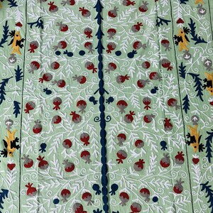 May include: A light green textile with an embroidered tree design. The tree has a dark blue trunk and branches, with red and gray fruit. White, yellow, and dark blue decorative elements are in the corners and edges. The text "AnokhiCreationStore" is at the bottom.