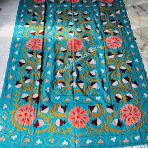 May include: A rectangular teal textile featuring intricate hand-embroidered floral patterns in shades of coral, dark maroon, and mustard yellow. The design includes large circular blossoms and small bud motifs arranged in a symmetrical layout with the text AnokhiCreationStore visible in the centre.