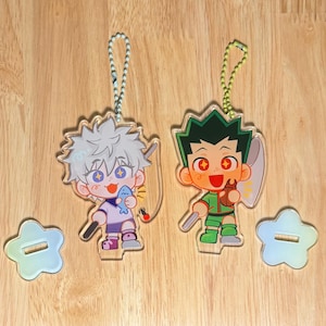 May include: Two acrylic anime character keychains. One keychain features a character with white hair holding a fish, the other features a character with green hair holding a fishing rod. Both have star-shaped stands.