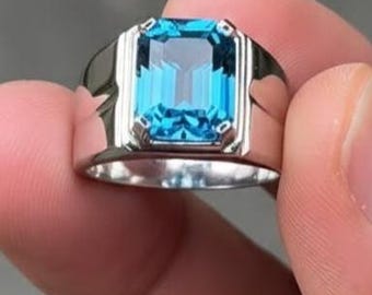 May include: A silver ring featuring a large, rectangular, bright blue gemstone. The ring has a classic, rectangular design with a polished finish. The gemstone is the focal point, showcasing its vibrant color and clarity. A piece of jewelry.
