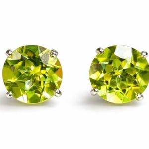 Può includere: Un paio di orecchini a lobo rotondi in peridoto verde chiaro. Ogni orecchino presenta una gemma sfaccettata incastonata in una montatura argentata a quattro griffe. Gli orecchini sono esposti su sfondo bianco.