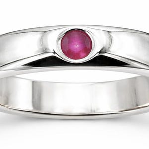 May include: A polished silver ring with a round, vibrant red gemstone set in the center. The ring has a smooth, rounded band and a sleek, modern design. The gemstone is approximately 0.12 inches in diameter.