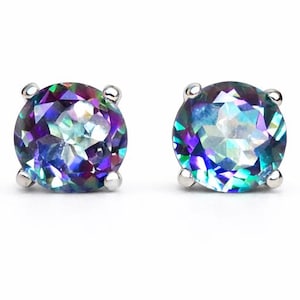 Puede incluir: Un par de pendientes de botón redondos con piedras preciosas iridiscentes. Las piedras muestran una mezcla de tonos azules, morados y verdes, engastadas en metal plateado. Los pendientes se muestran sobre un fondo blanco.