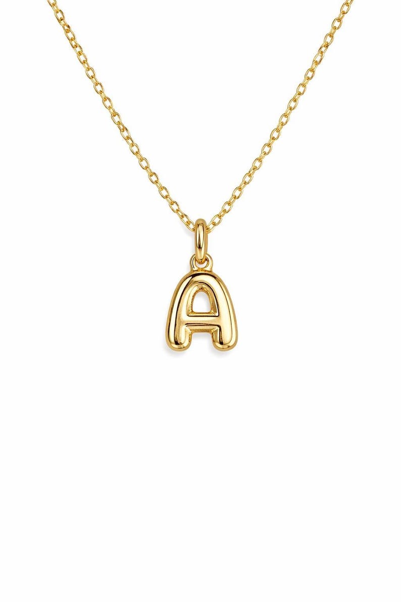 May include: A gold-colored necklace featuring a pendant in the shape of the letter "A". The pendant is a bold, rounded font and hangs from a delicate chain. The necklace is likely made of gold-plated metal.