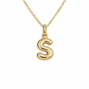 May include: A gold-colored necklace featuring a pendant in the shape of the letter "S". The pendant is a bold, rounded design, suspended from a delicate chain. The necklace is a simple yet elegant piece of jewelry.
