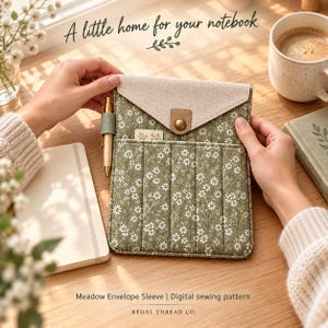 May include: A sage green fabric notebook sleeve featuring a white floral pattern, a beige envelope-style flap with a brass snap closure, and a side pen loop. The sleeve includes the text A little home for your notebook and Meadow Envelope Sleeve.