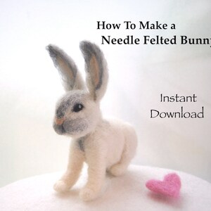 May include: A white needle felted bunny with gray ears and a pink heart. The bunny is sitting on a white surface. The text "How To Make a Needle Felted Bunny" and "Instant Download" is visible in the image.