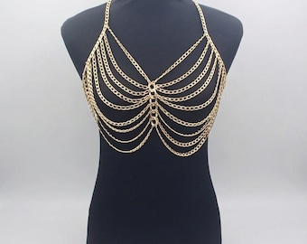 May include: Gold-colored chainmail top with a halter neck design. The top is made of multiple strands of delicate chains, creating a layered effect. The chains are connected at the neckline and center, forming a unique and eye-catching piece of body jewelry.