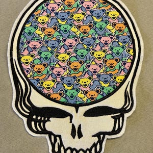 May include: Embroidered patch featuring a skull design with a colorful pattern of dancing bears inside the skull's head. The bears are in various colors, including yellow, blue, orange, pink, and green. The skull is white with black outlines.