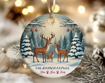 May include: A round Christmas ornament featuring a winter scene with a family of deer in a snowy forest. The ornament has a gold ribbon for hanging and includes the text "THE JOHNSON FAMILY" and names "Mike, John, Sally".