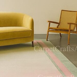 Pu&ograve; includere: Un divano giallo senape e una sedia in legno con schienale intrecciato poggiano su un tappeto chiaro con una striscia rosa e verde. Il tappeto &egrave; davanti alla sedia e al divano. La stanza ha un design minimalista.