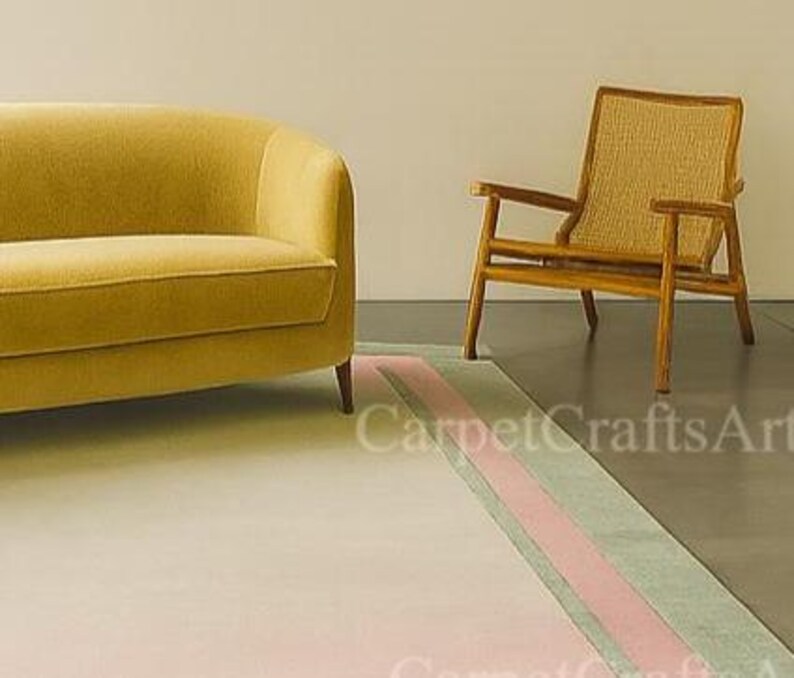 Pu&ograve; includere: Un divano giallo senape e una sedia in legno con schienale intrecciato poggiano su un tappeto chiaro con una striscia rosa e verde. Il tappeto &egrave; davanti alla sedia e al divano. La stanza ha un design minimalista.