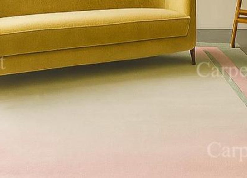 Pu&ograve; includere: Un tappeto dai colori pastello con un effetto sfumato, che passa dal rosa chiaro al bianco crema. Un divano giallo &egrave; parzialmente visibile sullo sfondo. Il tappeto ha un bordo con strisce rosa e verdi.