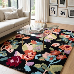 May include: A black area rug with a colorful floral pattern. The rug features large, stylized flowers in shades of red, orange, blue, and green. The rug is placed in a living room with a glass coffee table.