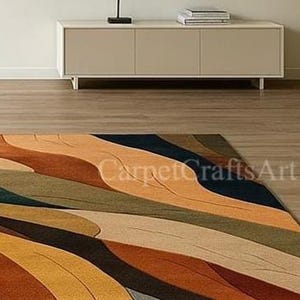 May include: A rectangular rug with an abstract design in shades of orange, brown, teal, and beige. The rug has a wave-like pattern and is on a wooden floor. The text "CarpetCraftsArt" is visible on the rug. The rug is suitable for a living room.