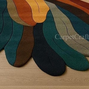 May include: A close-up of a colourful rug with an abstract design. The rug features curved, petal-like shapes in shades of teal, brown, orange, and yellow. The text "CarpetCraftsArt" is visible on the rug.