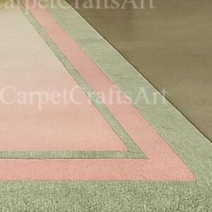 Pu&ograve; includere: Vista angolare di un tappeto rettangolare con centro rosa, bordato da una fascia e frange verde chiaro. Il tappeto ha un aspetto sbiadito, con il testo "CarpetCraftsArt" visibile nell'angolo.