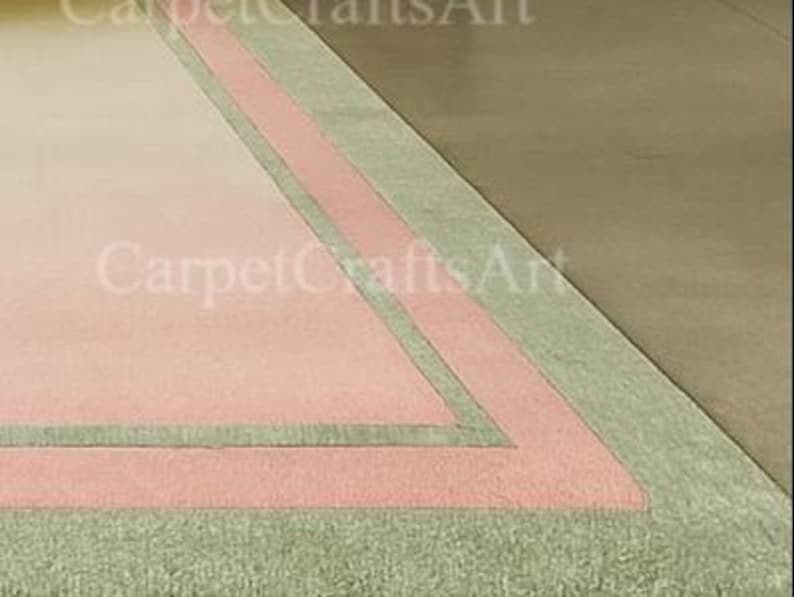 Pu&ograve; includere: Vista angolare di un tappeto rettangolare con centro rosa, bordato da una fascia e frange verde chiaro. Il tappeto ha un aspetto sbiadito, con il testo "CarpetCraftsArt" visibile nell'angolo.