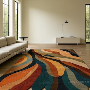 May include: A large, colourful area rug with an abstract design. The rug features flowing, feather-like shapes in shades of orange, brown, teal, and blue. The rug is placed on a wooden floor in a modern living room setting.