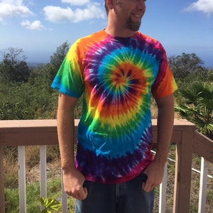 Puede incluir: Un hombre con una camiseta tie-dye de colores con un patr&oacute;n en espiral en tonos de azul, verde, amarillo, naranja, rojo y morado.