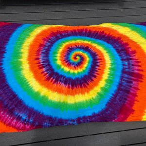 Pu&ograve; includere: Un arazzo tie-dye colorato con un grande motivo a spirale in tonalit&agrave; di rosso, arancione, giallo, verde, blu e viola.