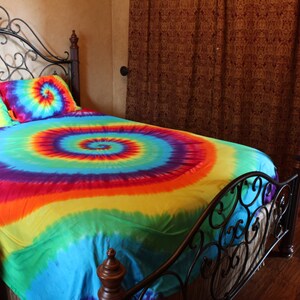 Pu&ograve; includere: Un letto con una struttura in metallo nero e un copripiumino e federe tie-dye. Il copripiumino &egrave; un arcobaleno di colori con un motivo a spirale.