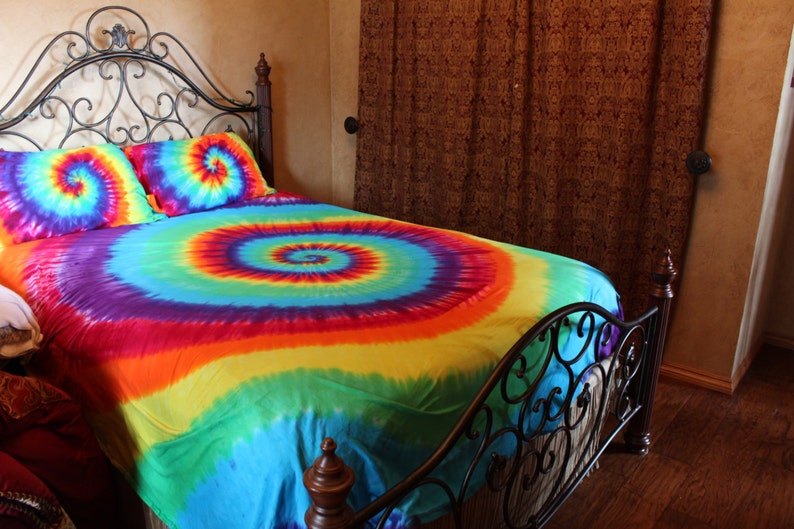 Pu&ograve; includere: Un letto con una struttura in metallo nero e un copripiumino e federe tie-dye. Il copripiumino &egrave; un arcobaleno di colori con un motivo a spirale.