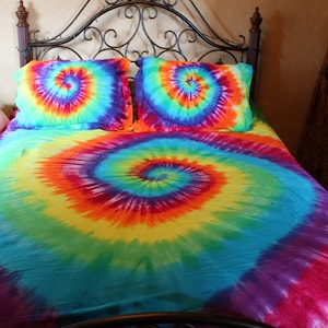 Pu&ograve; includere: Un letto con un copripiumino tie-dye colorato e federe abbinate. Il copripiumino presenta un grande motivo a spirale in tonalit&agrave; di blu, verde, giallo, arancione e rosso.