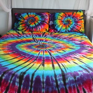 May include: A tie-dye bedspread with a large, colorful swirl pattern in shades of blue, purple, red, orange, yellow, and black. The bedspread is on a bed with two matching tie-dye pillowcases.
