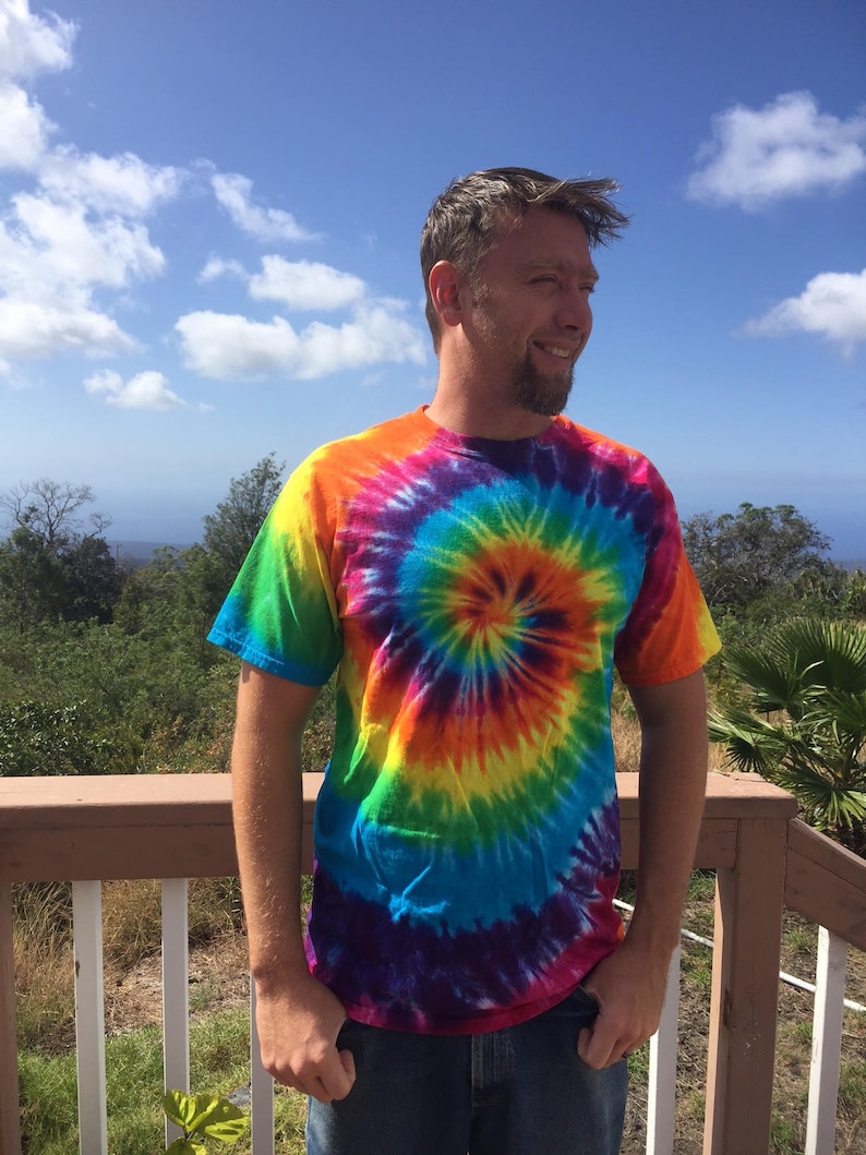 Puede incluir: Un hombre con una camiseta tie-dye de colores con un patr&oacute;n en espiral en tonos de azul, verde, amarillo, naranja, rojo y morado.