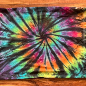 May include: A black fabric with a colorful tie-dye pattern in shades of purple, blue, green, orange, and yellow. The pattern is a spiral design.