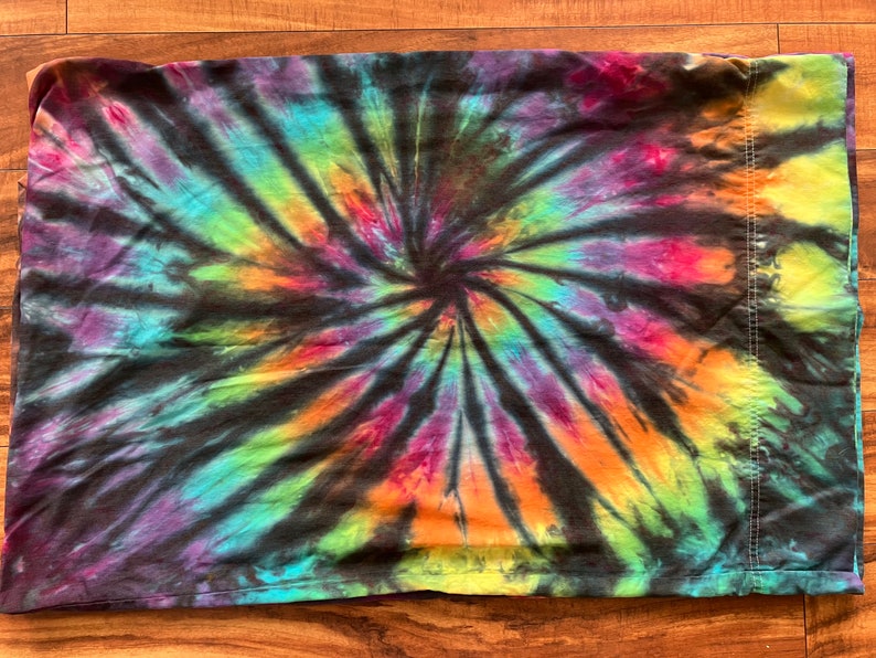 May include: A black fabric with a colorful tie-dye pattern in shades of purple, blue, green, orange, and yellow. The pattern is a spiral design.