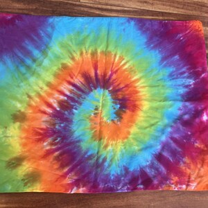 Könnte beinhalten: Rechteckiger Stoff mit Batikmuster und Spiralmuster. Das Design zeigt eine lebendige Farbpalette, darunter Lila, Blau, Grün, Gelb, Orange und Rosa. Die Farben verschmelzen kreisförmig und erzeugen einen psychedelischen Effekt.