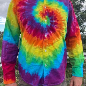 May include: A long-sleeved button-down shirt with a colorful tie-dye pattern in shades of red, orange, yellow, green, blue, and purple. The shirt has a spiral design.