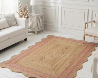 May include: A rectangular jute rug with a scalloped edge and a pink border. The rug is placed on a white wooden floor in a room with white walls, a white sofa, and a white chair. The rug's dimensions are not visible.