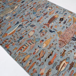 Könnte beinhalten: Rechteckiger, hellblauer Teppich mit einem sich wiederholenden Muster aus bunten Fischen. Die Fische variieren in Größe und Design, mit Farbtönen von Orange, Braun und Blau. Der Teppich ist wahrscheinlich aus gewebtem Material.