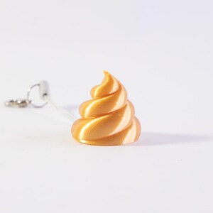 Op de afbeelding: Een goudkleurige, 3D-geprinte poep emoji-bedel met een wit koord en zilverkleurige sluiting. De bedel is een grillig accessoire, perfect om aan een sleutelhanger of tas te bevestigen. De emoji is een humoristisch en speels ontwerp.